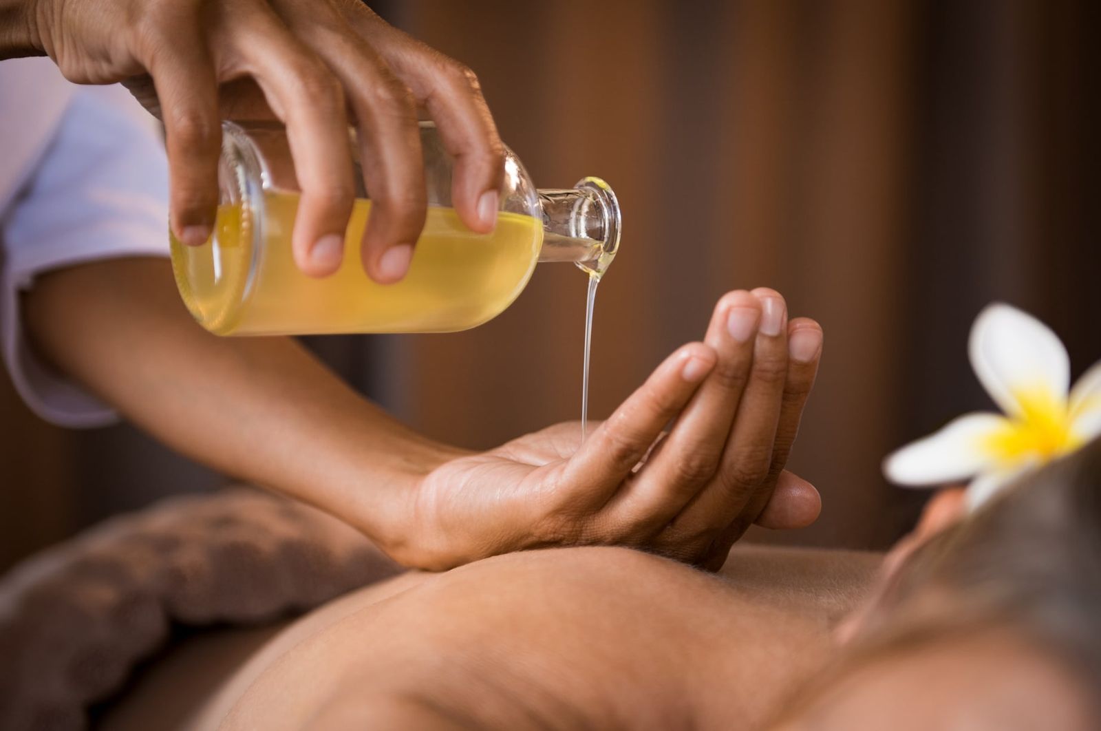 Therapist pouring warm herbal oil for an Abhyanga massage